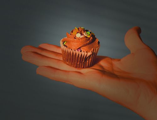 A mini cupcake perched in the palm of a hand. 