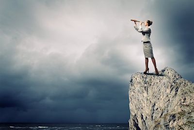 Image of businesswoman looking in telescope standing atop of rock